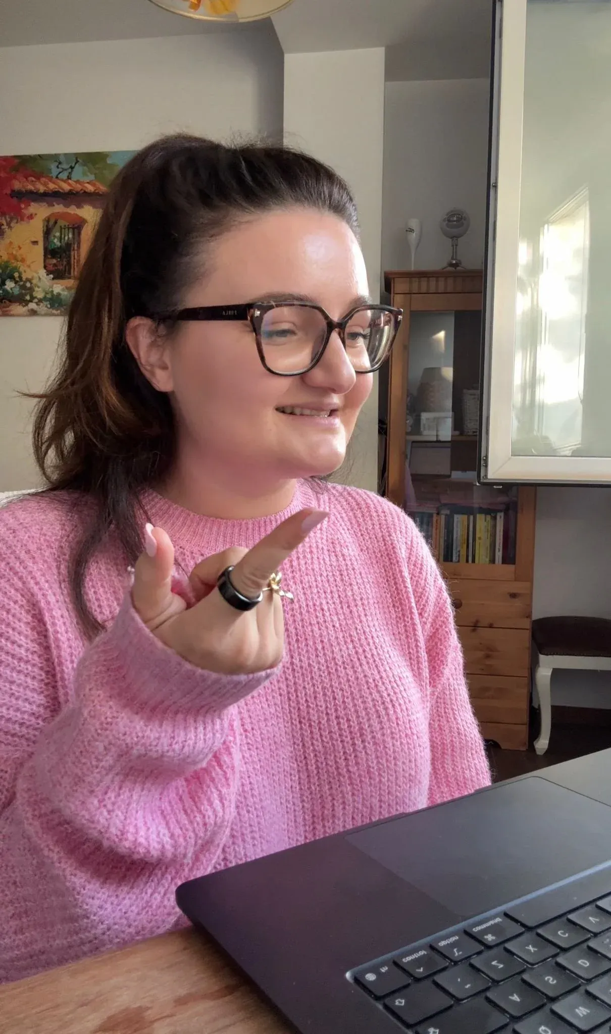 Sabina zâmbind la laptop, într-un pulover roz